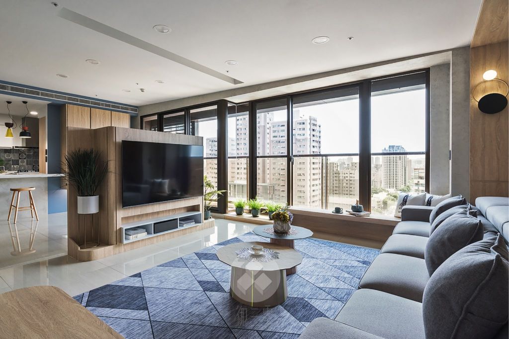 一個現代化的客廳，包含沙發、電視和窗邊植物，空間寬敞明亮，窗外可見城市景觀，還有一個微傾斜的天花板非常有特色。